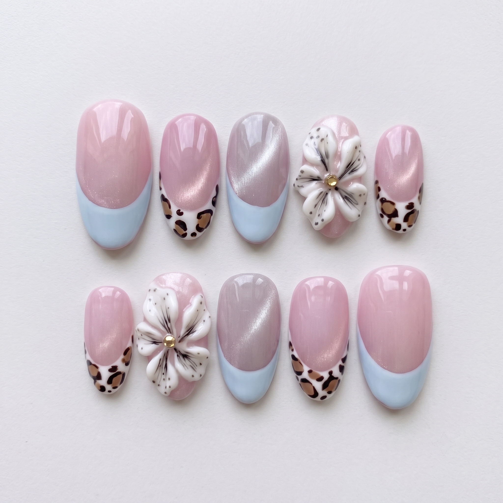Pink cat-eye press-on nails with blue French tips, leopard print accents, and 3D white flowers.