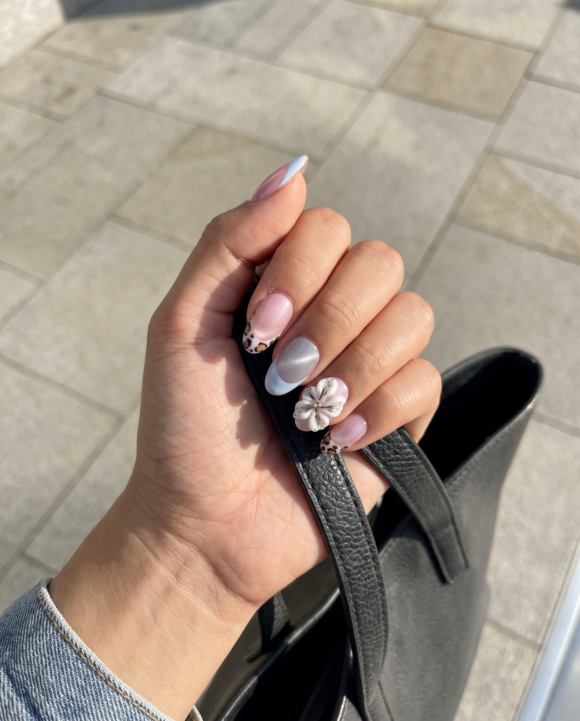 Pink cat-eye press-on nails with blue French tips, leopard print accents, and 3D white flowers.
