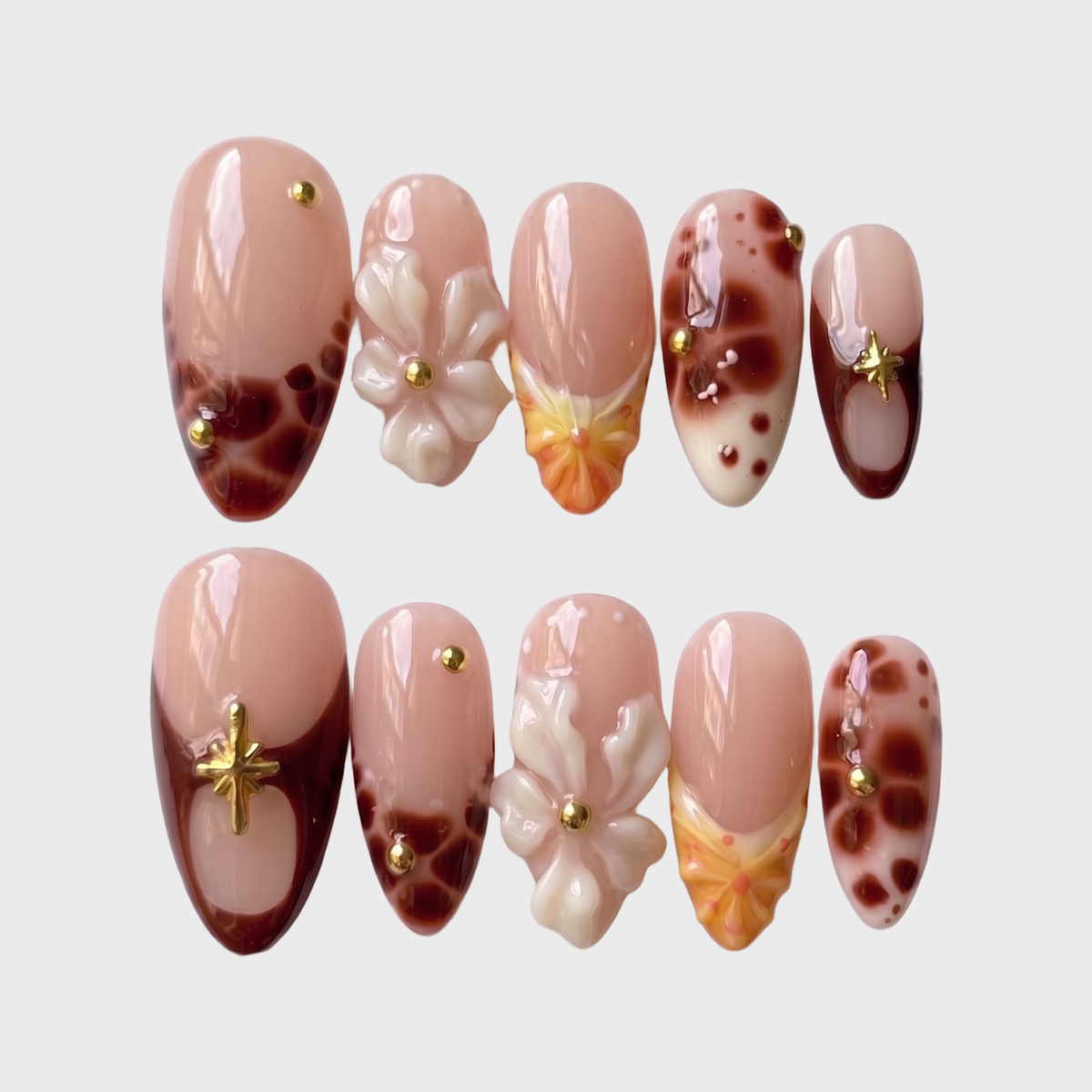 A set of press-on nails featuring tortoiseshell patterns, 3D white flowers, gold star charms, and yellow gradient details on a nude base.