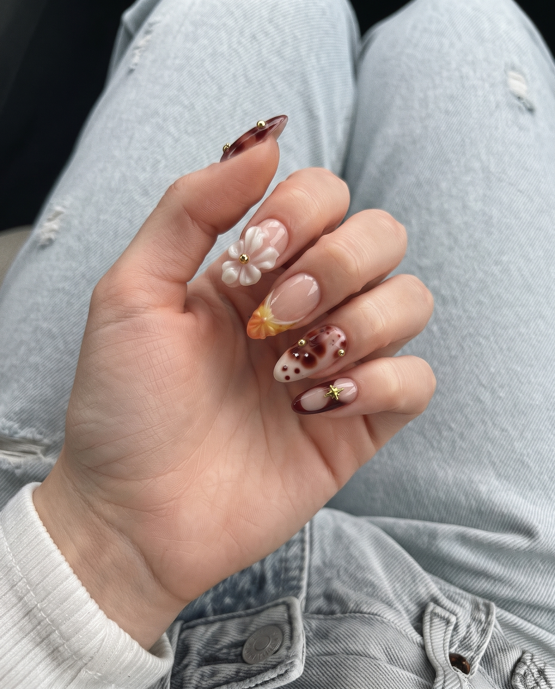 A set of press-on nails featuring tortoiseshell patterns, 3D white flowers, gold star charms, and yellow gradient details on a nude base.