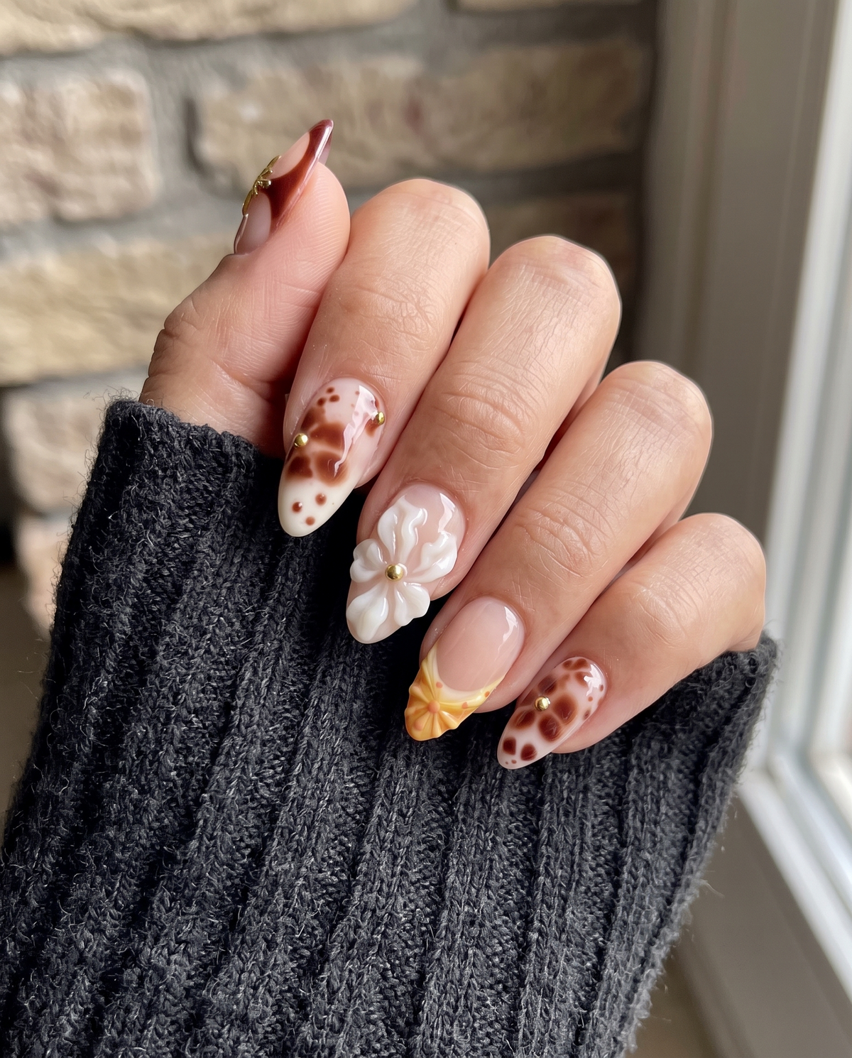A set of press-on nails featuring tortoiseshell patterns, 3D white flowers, gold star charms, and yellow gradient details on a nude base.