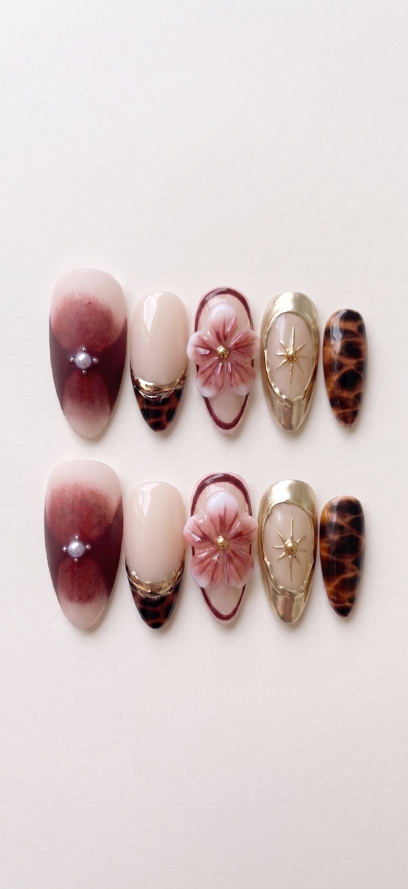 A set of press-on nails featuring 3D floral designs, tortoise shell patterns, and burgundy ombre with pearl accents.