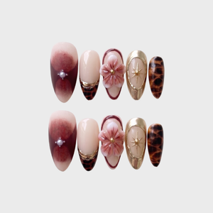 A set of press-on nails featuring 3D floral designs, tortoise shell patterns, and burgundy ombre with pearl accents.