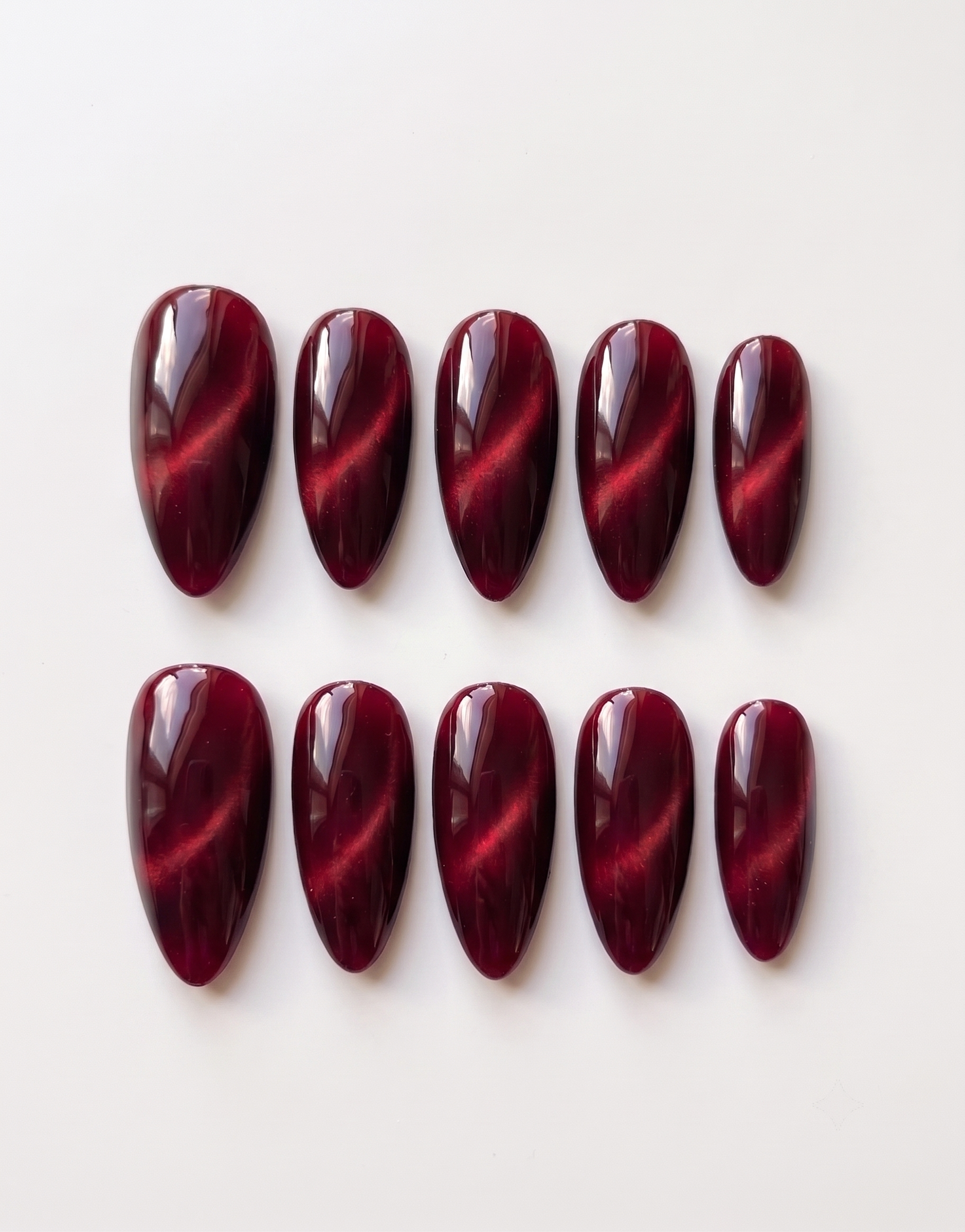 Ten almond-shaped press-on nails in a deep burgundy color with a magnetic cat eye shimmer effect.