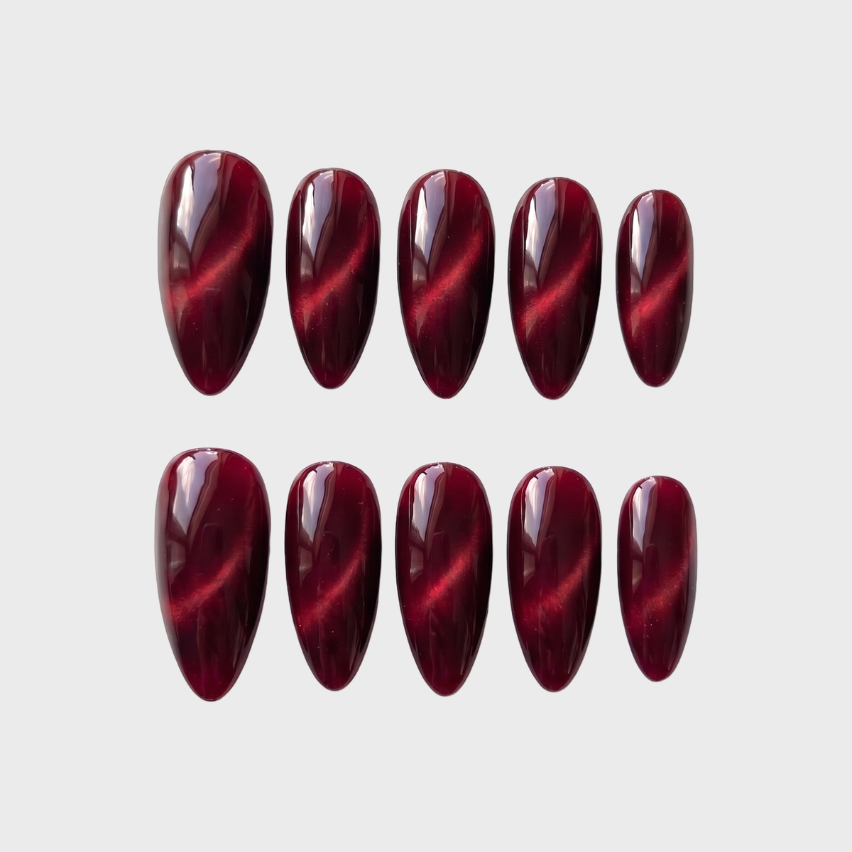 Ten almond-shaped press-on nails in a deep burgundy color with a magnetic cat eye shimmer effect.