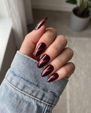 Ten almond-shaped press-on nails in a deep burgundy color with a magnetic cat eye shimmer effect.