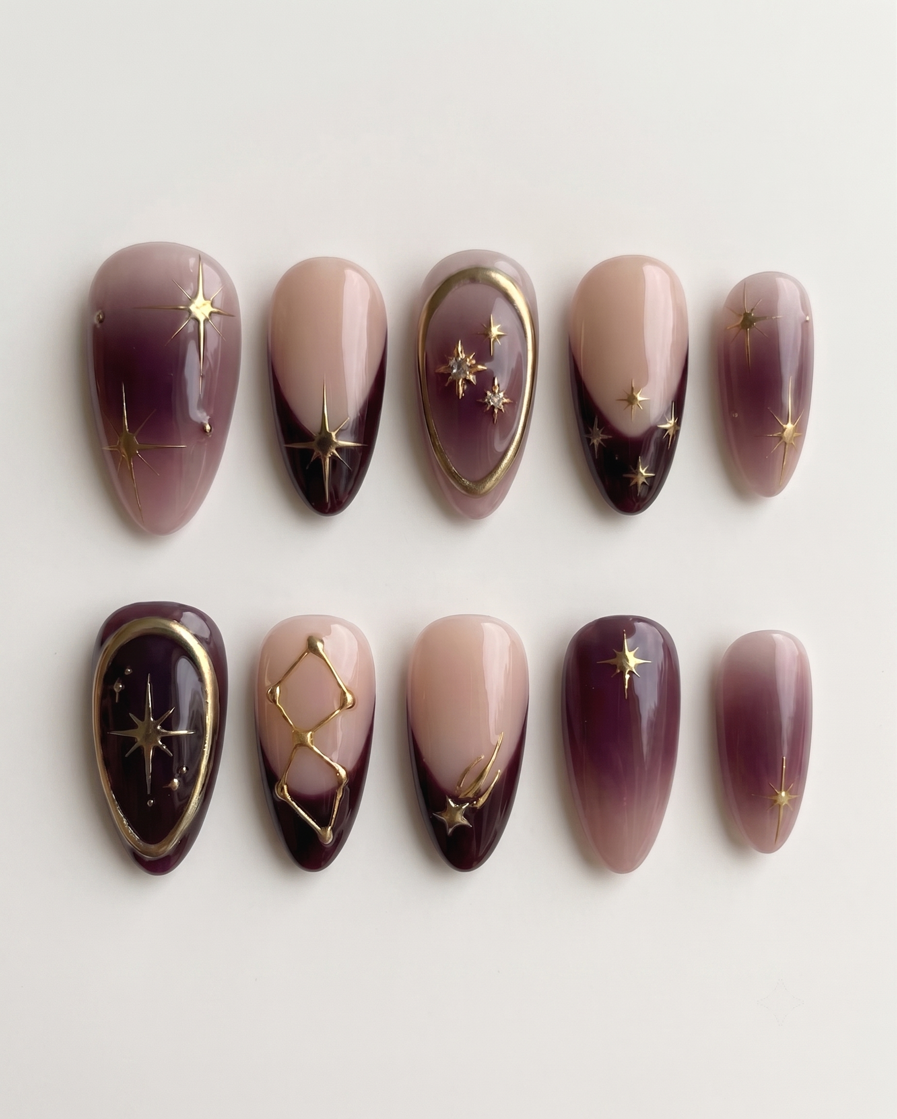 Celestial burgundy French press-on nails with gold star and constellation designs.