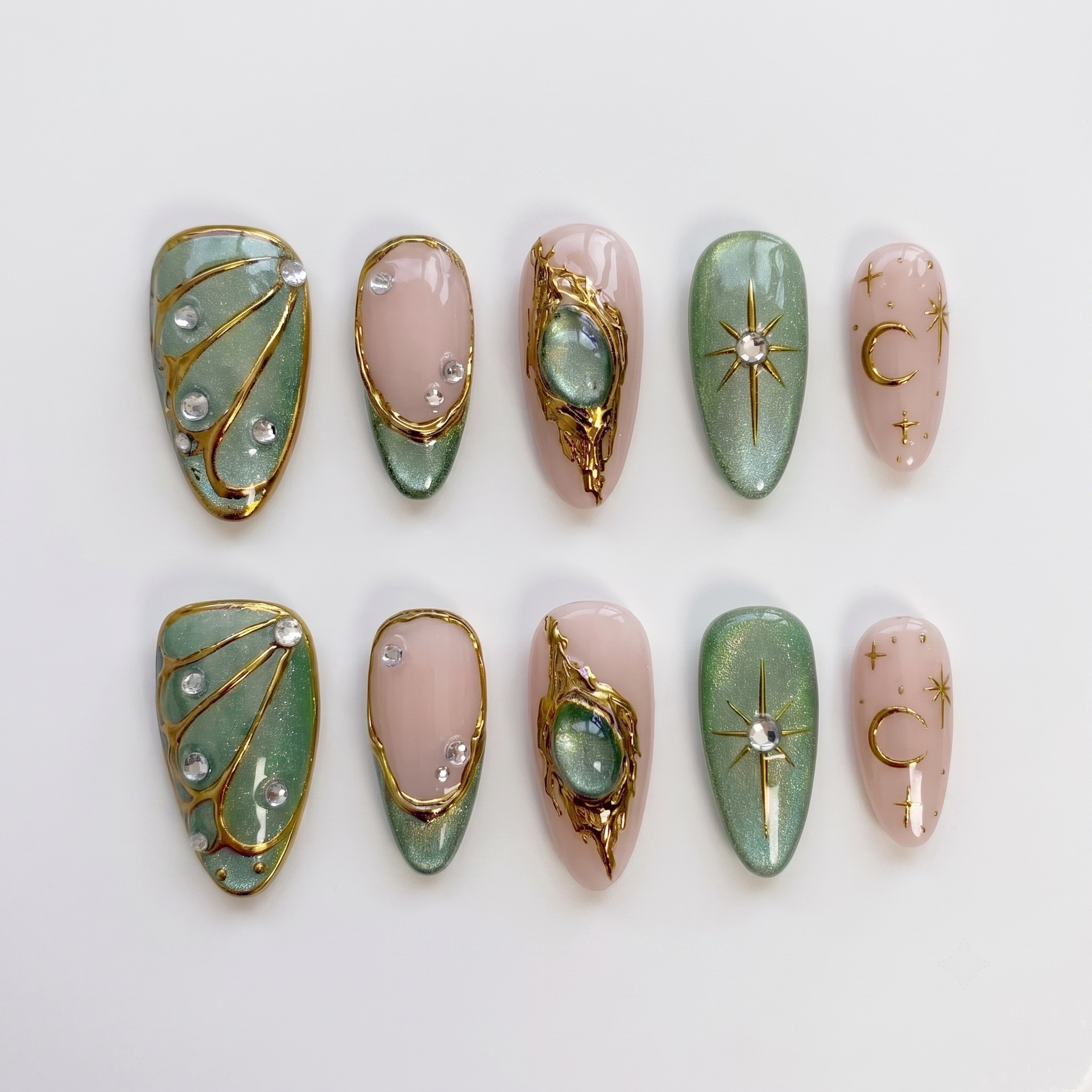 Sage green and pink press-on nails featuring gold celestial stars, crescent moons, butterfly wings, and rhinestone accents.