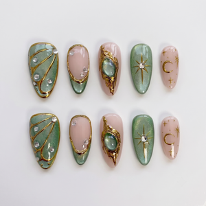 Sage green and pink press-on nails featuring gold celestial stars, crescent moons, butterfly wings, and rhinestone accents.