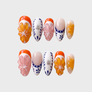 A set of press-on nails featuring 3D orange and pink fruit slices, blue floral patterns on white, and French tips.