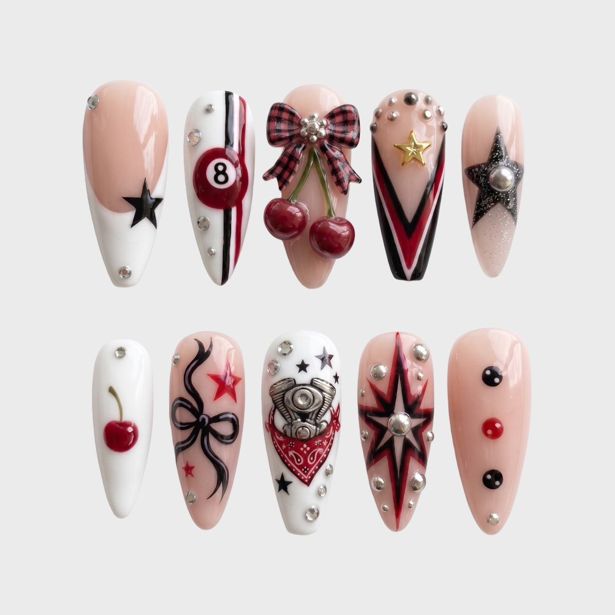 A set of almond-shaped press-on nails with red and black grunge designs including 3D cherries, an 8-ball, stars, and metallic studs.