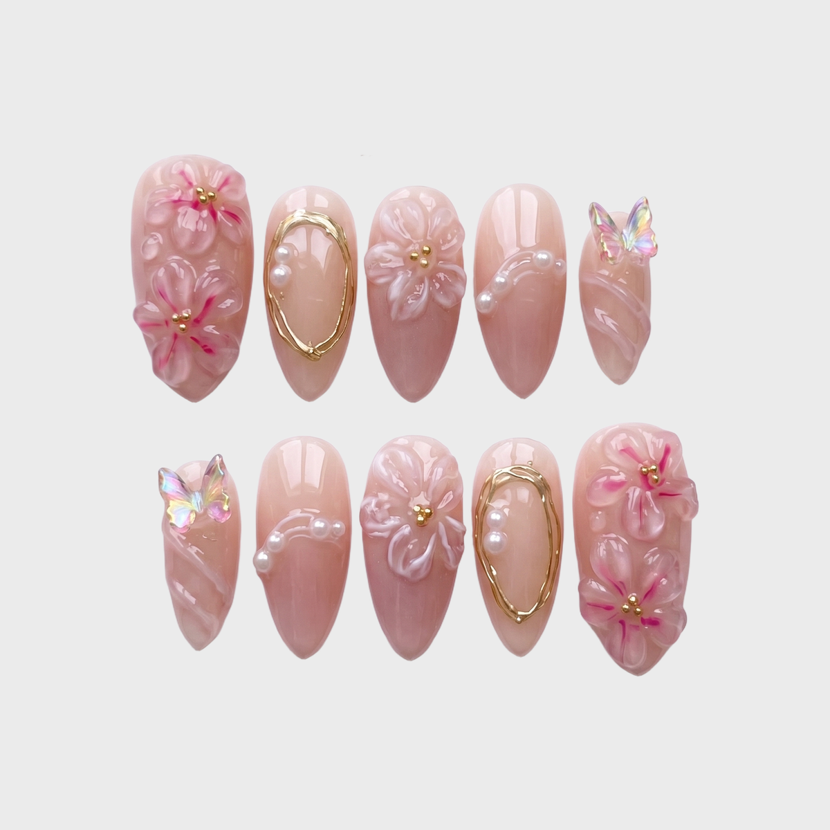 A set of pink press-on nails featuring 3D floral designs, iridescent butterfly charms, and gold wire accents.