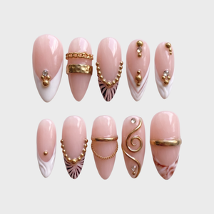 A set of pink and white press-on nails decorated with gold bands, chains, studs, zebra stripes, and rhinestones.