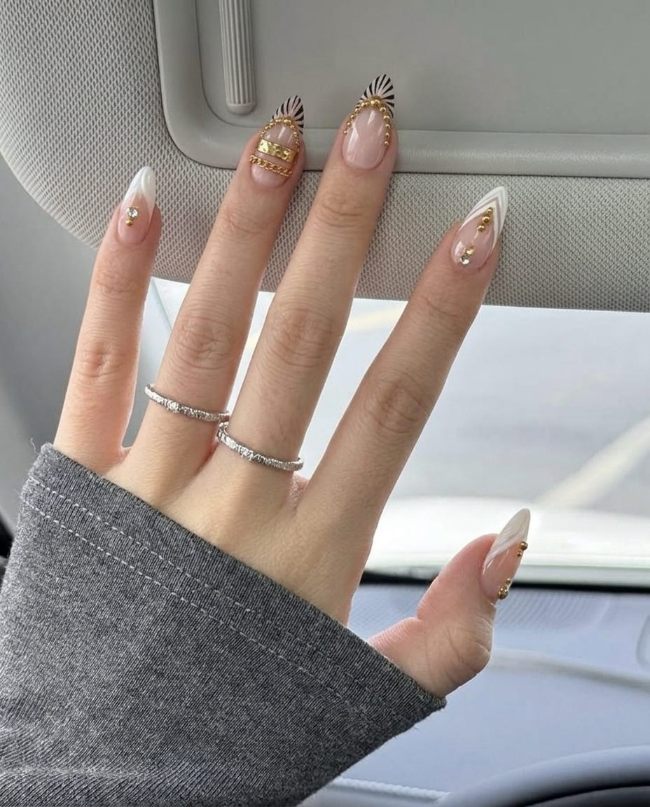 A set of pink and white press-on nails decorated with gold bands, chains, studs, zebra stripes, and rhinestones.