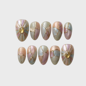 A set of iridescent press-on nails with gold kintsugi cracks and sunburst gemstone accents.
