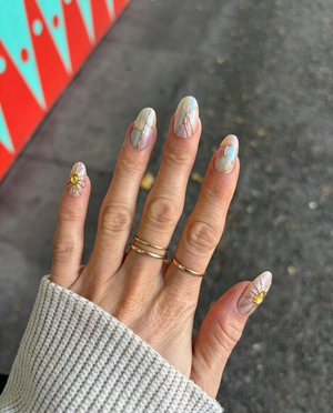 A set of iridescent press-on nails with gold kintsugi cracks and sunburst gemstone accents.