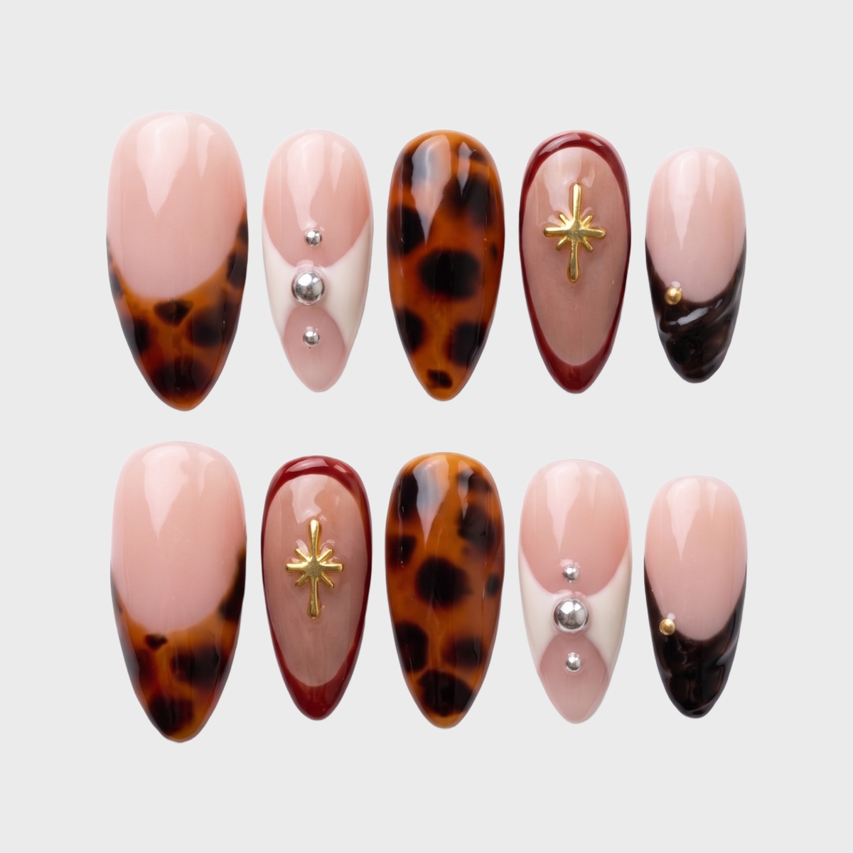 Tortoiseshell French tip press-on nails with gold star charms and silver studs.