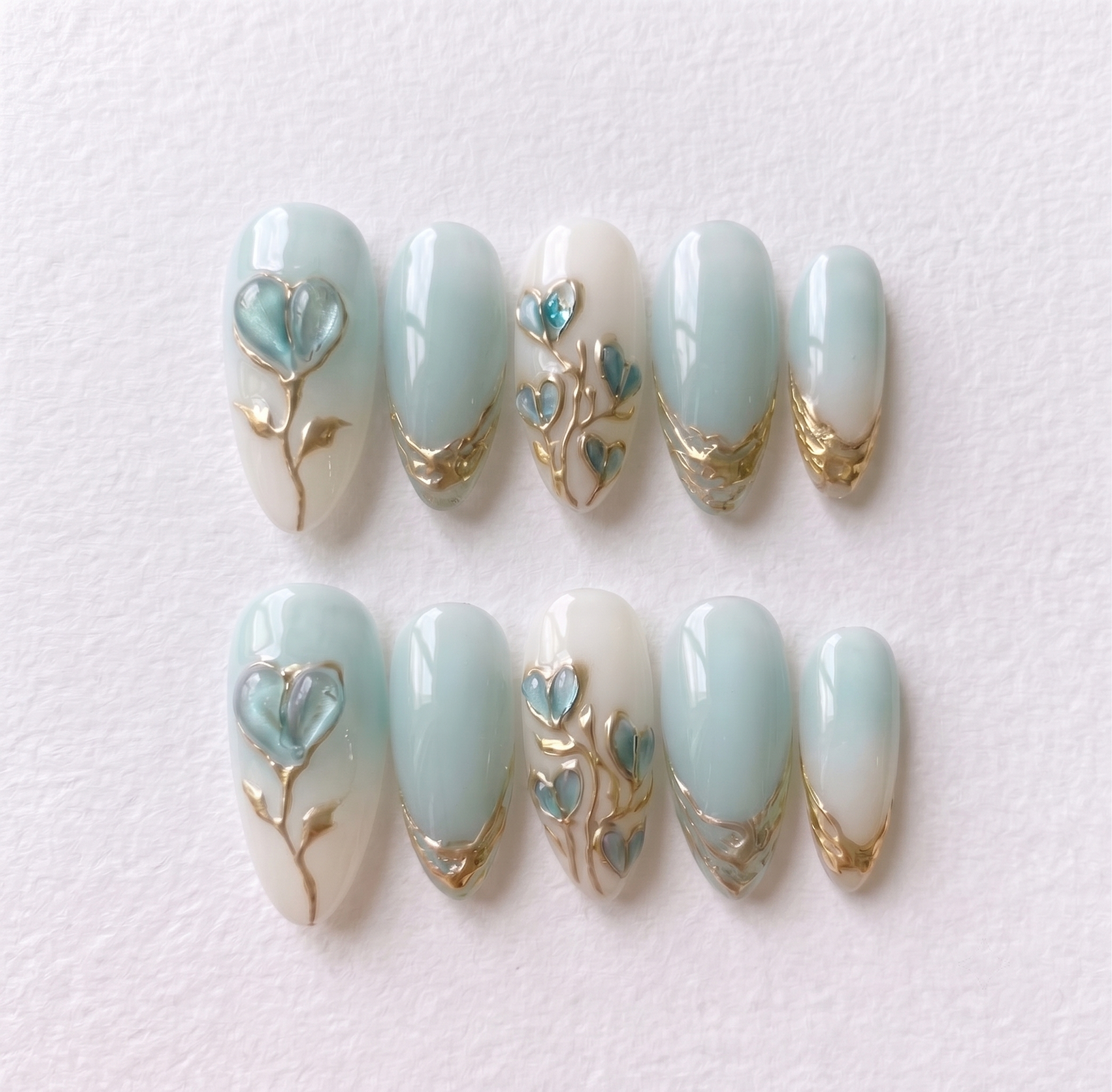 Mint blue and milky white ombré press-on nails with 3D heart-shaped floral details and metallic gold accents.