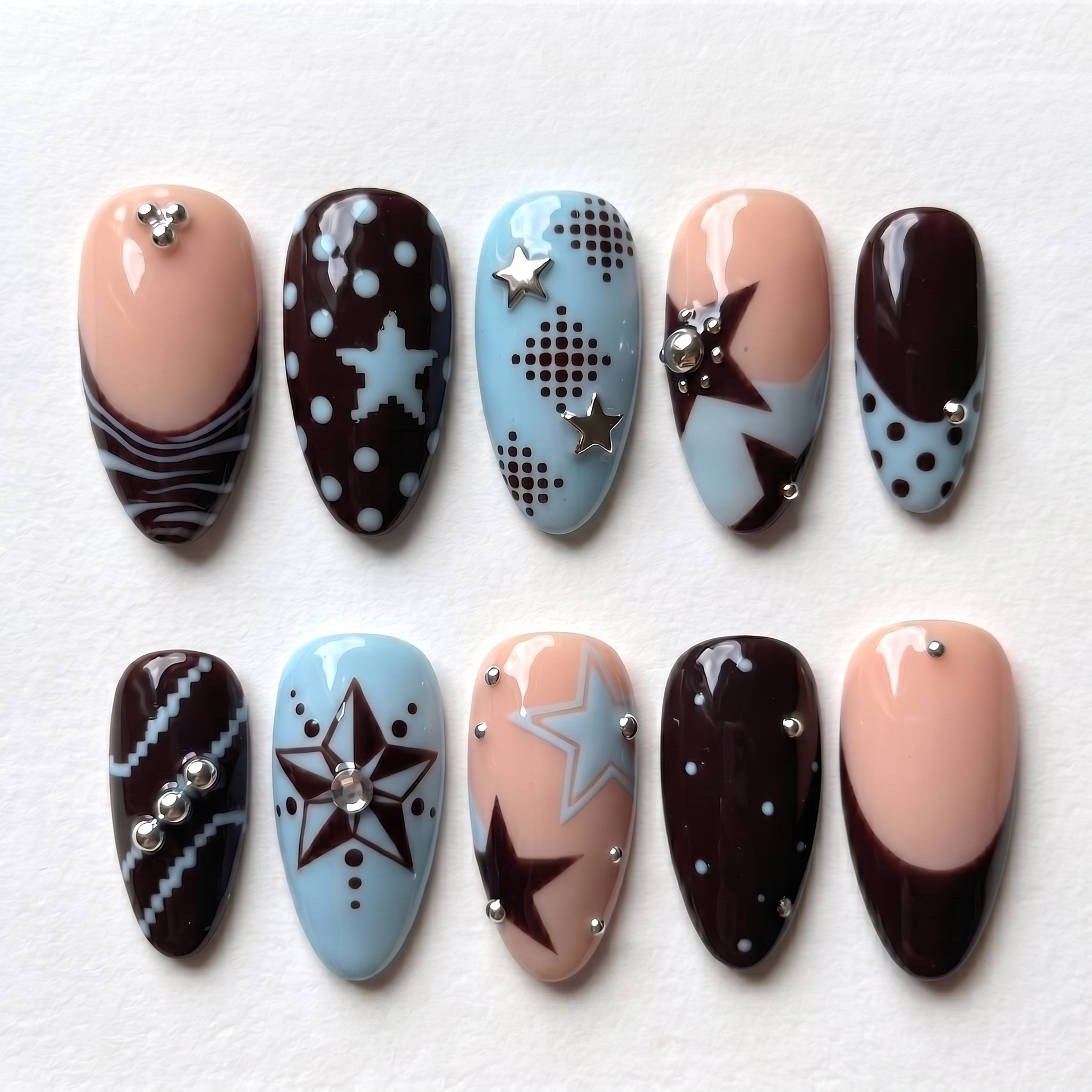 A set of press-on nails featuring mocha brown, baby blue, and nude colors with star and dot motifs and silver studs.