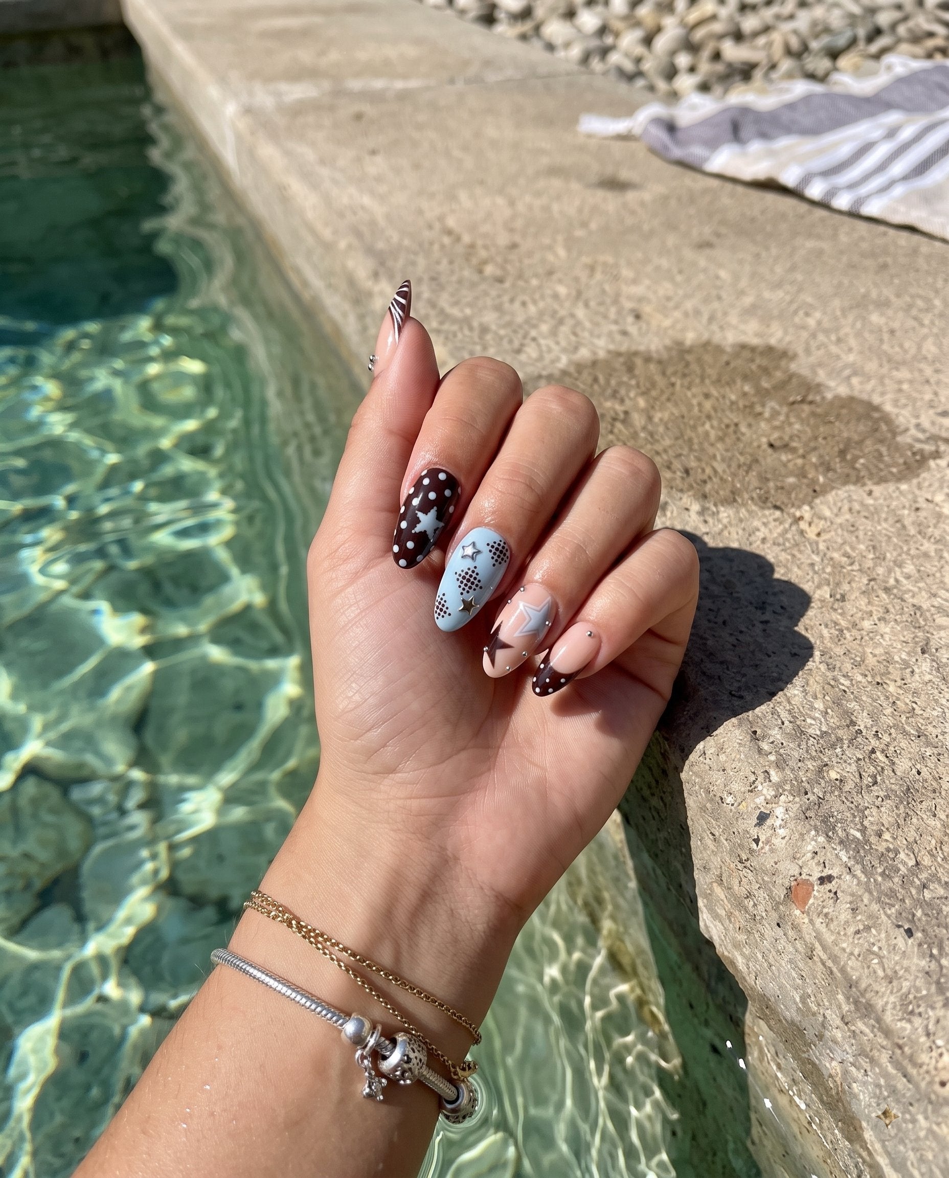 A set of press-on nails featuring mocha brown, baby blue, and nude colors with star and dot motifs and silver studs.