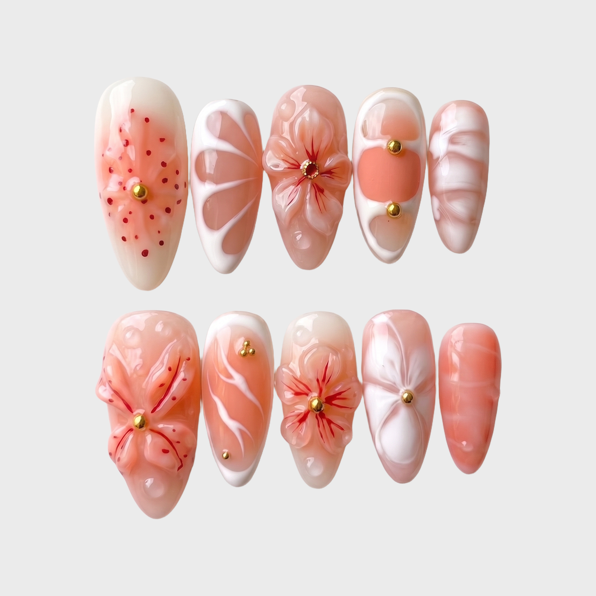 Peach press-on nails featuring 3D sculpted flowers, gold studs, white swirls, and a glossy finish.