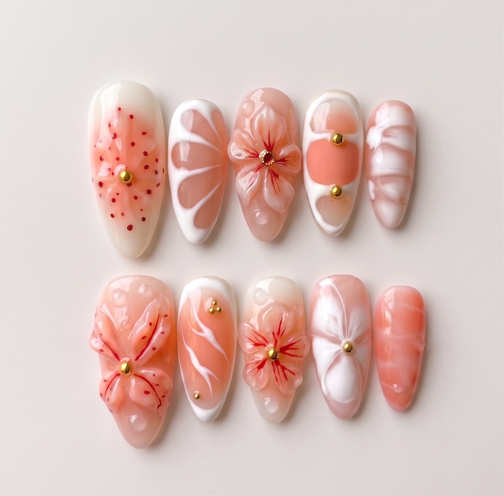 Peach press-on nails featuring 3D sculpted flowers, gold studs, white swirls, and a glossy finish.
