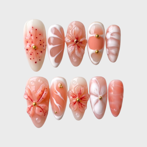 Peach press-on nails featuring 3D sculpted flowers, gold studs, white swirls, and a glossy finish.