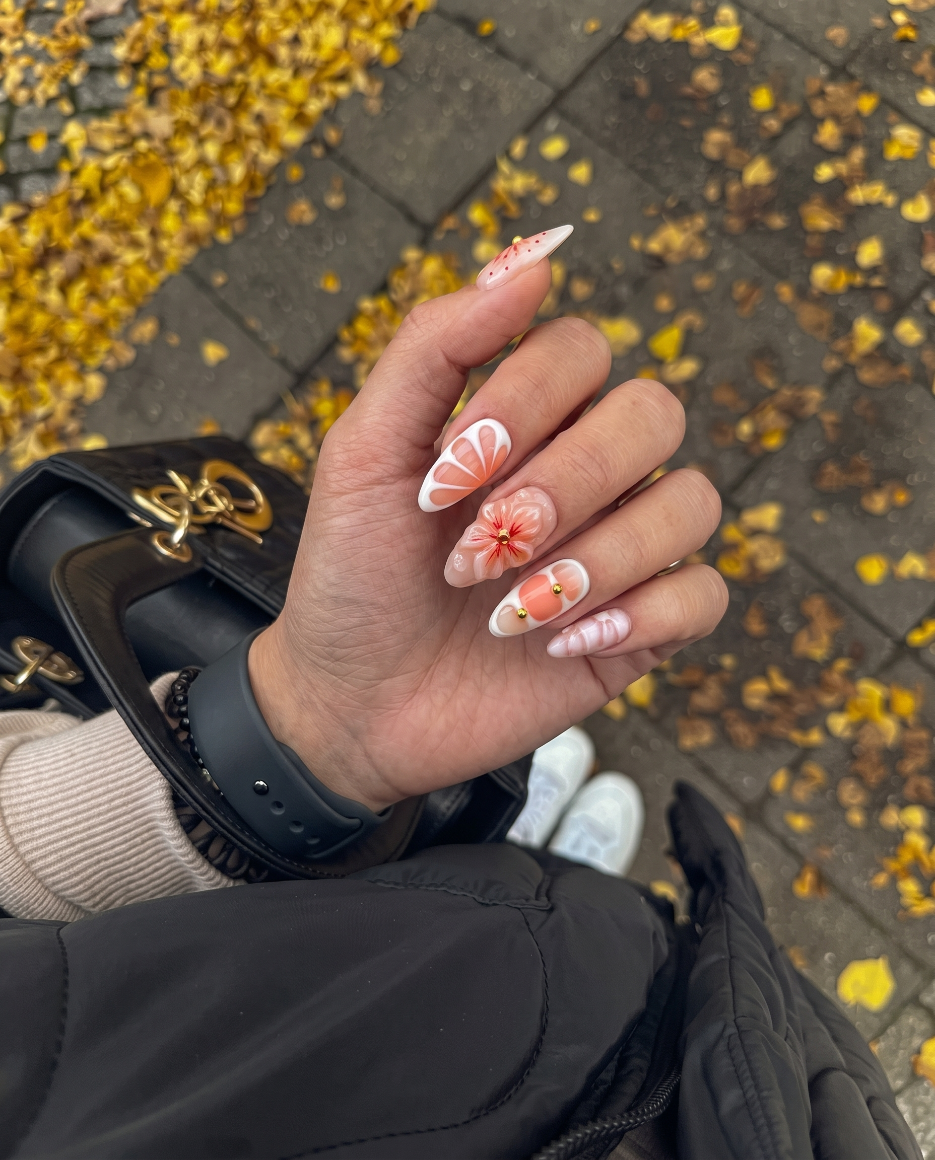 Peach press-on nails featuring 3D sculpted flowers, gold studs, white swirls, and a glossy finish.