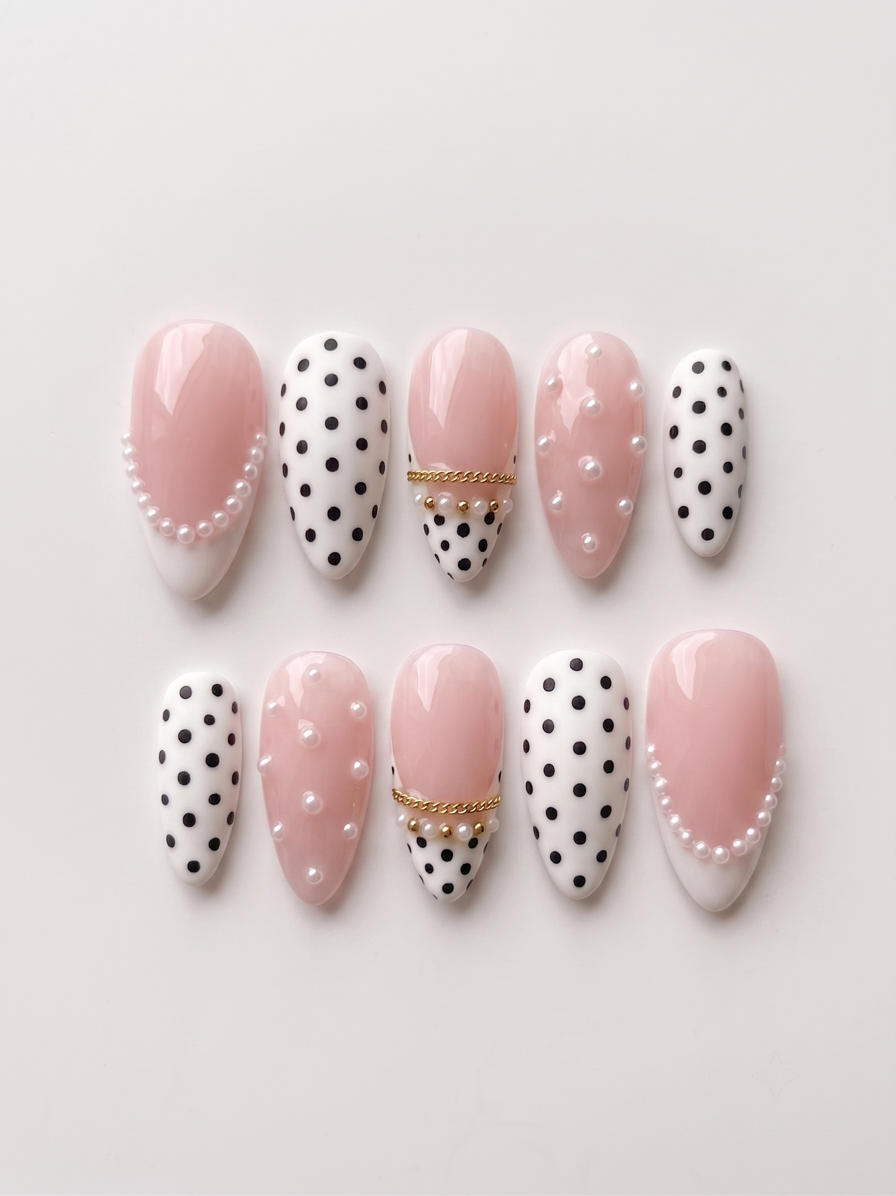 A set of Meevia Nails press-on nails featuring a mix of glossy pink bases, black polka dots on white, white pearl embellishments, and gold chain details.