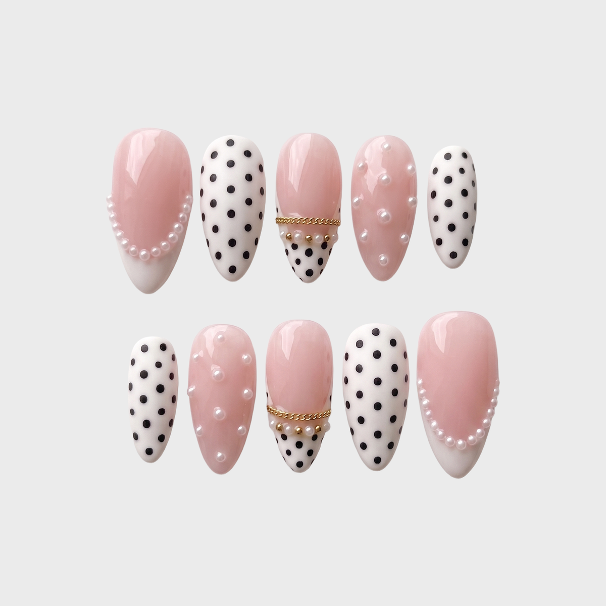 A set of Meevia Nails press-on nails featuring a mix of glossy pink bases, black polka dots on white, white pearl embellishments, and gold chain details.