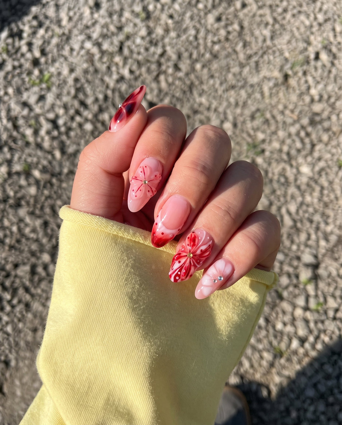 Set of press-on nails featuring red 3D floral designs, nautical charms, and rhinestone accents on a soft pink base.