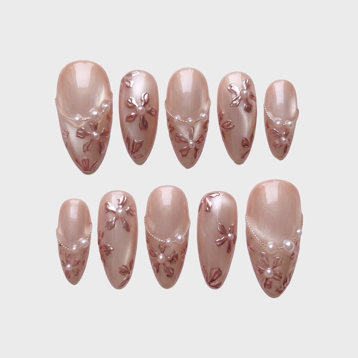 Rose gold press-on nails with 3D metallic floral details, pearl accents, and a shimmery finish.