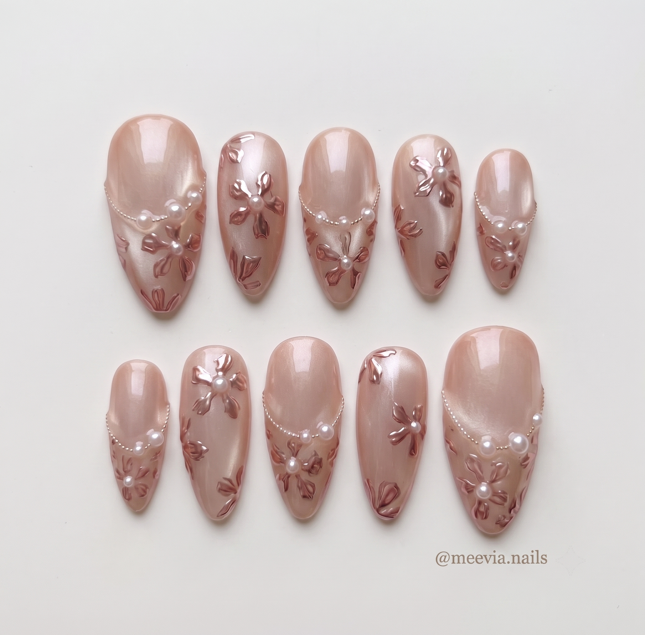 Rose gold press-on nails with 3D metallic floral details, pearl accents, and a shimmery finish.