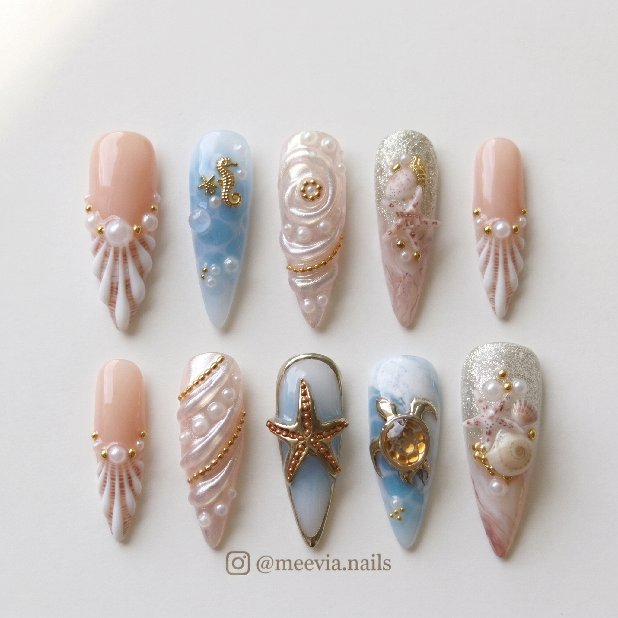 A set of stiletto press-on nails featuring ocean-themed designs with shells, pearls, starfish, and a sea turtle.