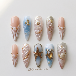 A set of stiletto press-on nails featuring ocean-themed designs with shells, pearls, starfish, and a sea turtle.