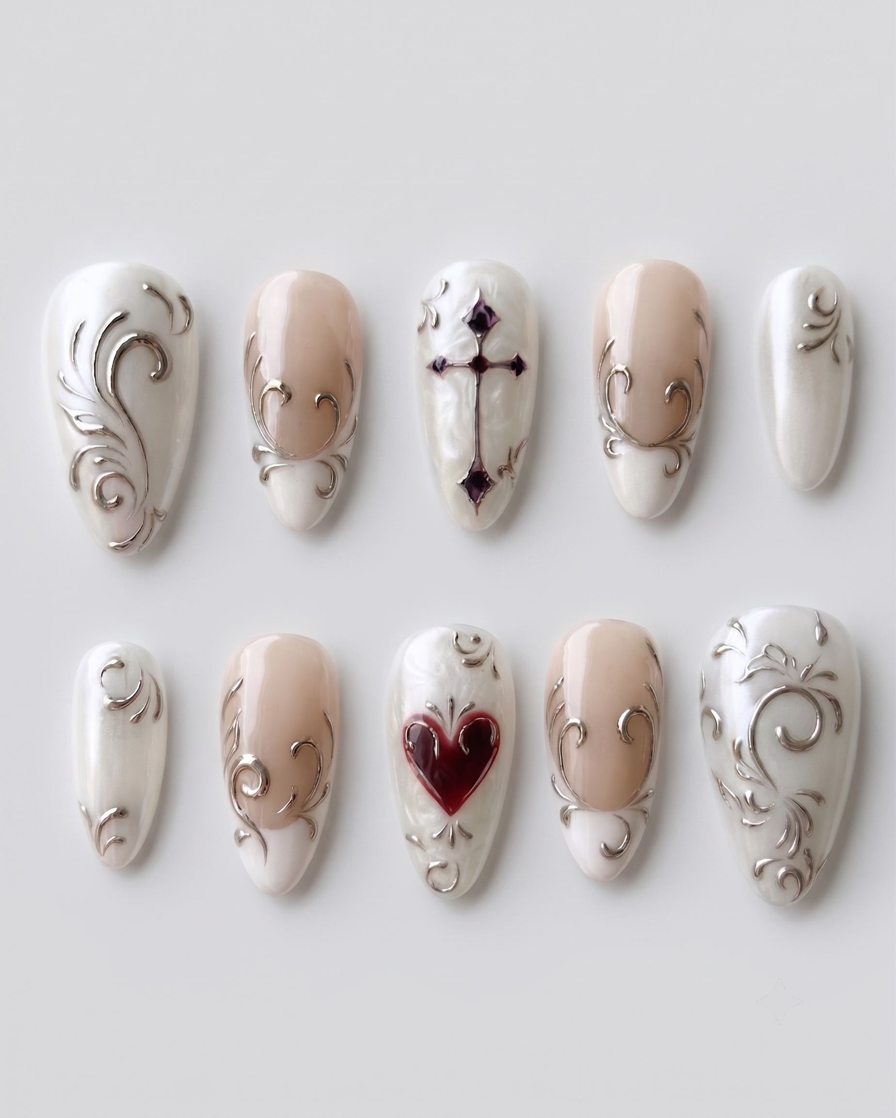 Pearl white press-on nails featuring metallic silver scrollwork, French tips, a dark red heart, and a gothic cross.
