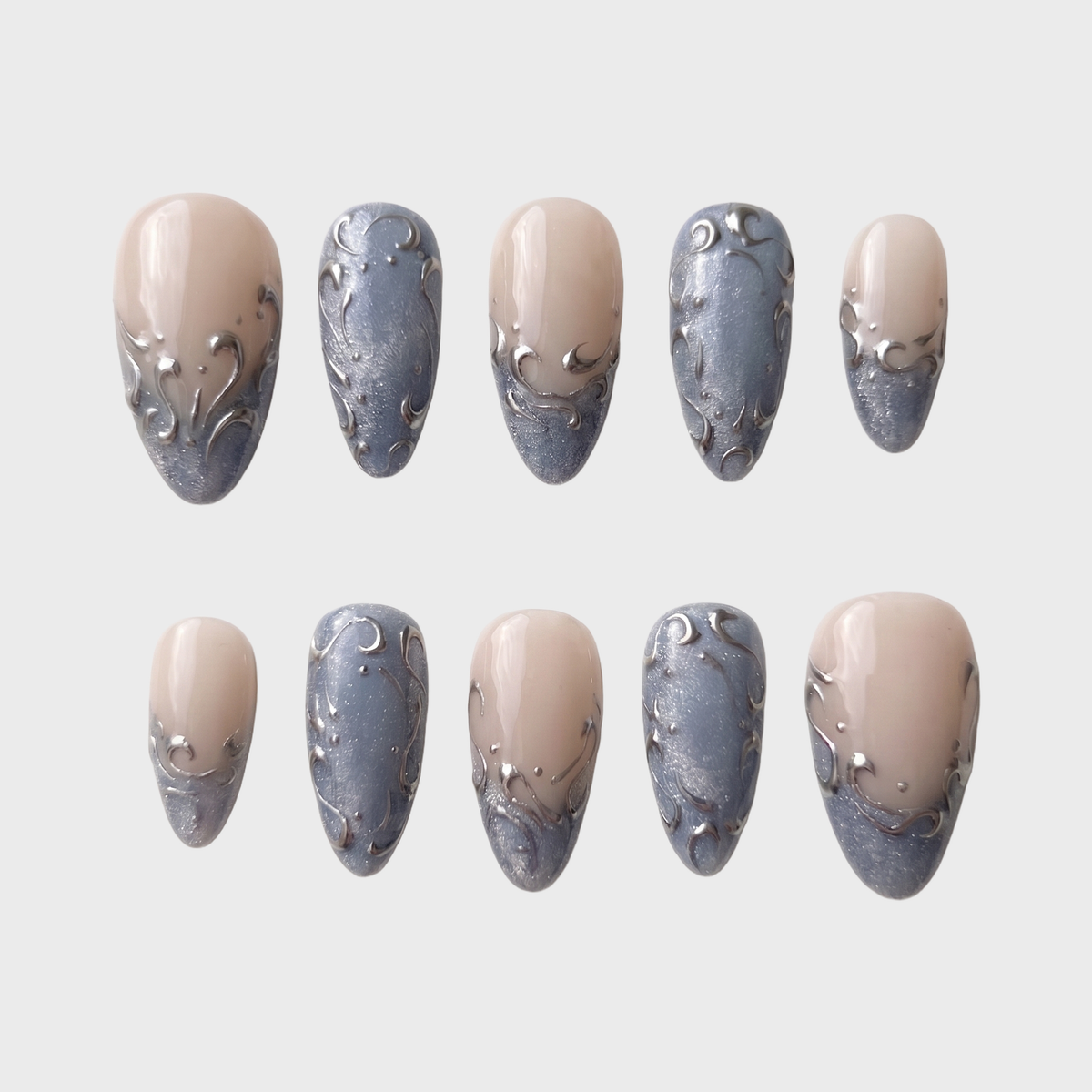 A set of press-on nails featuring a nude base, shimmering blue-grey French tips, and raised silver filigree swirl designs.