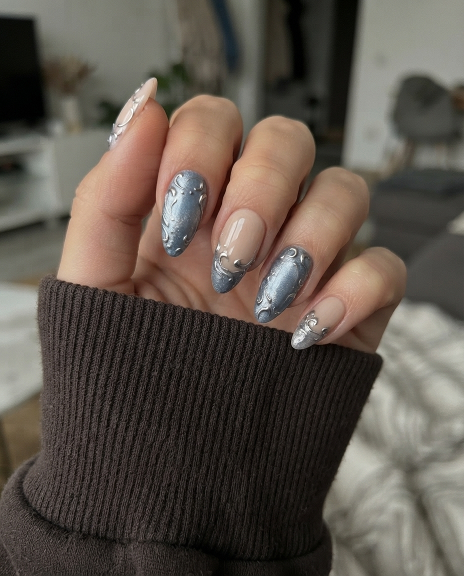 A set of press-on nails featuring a nude base, shimmering blue-grey French tips, and raised silver filigree swirl designs.