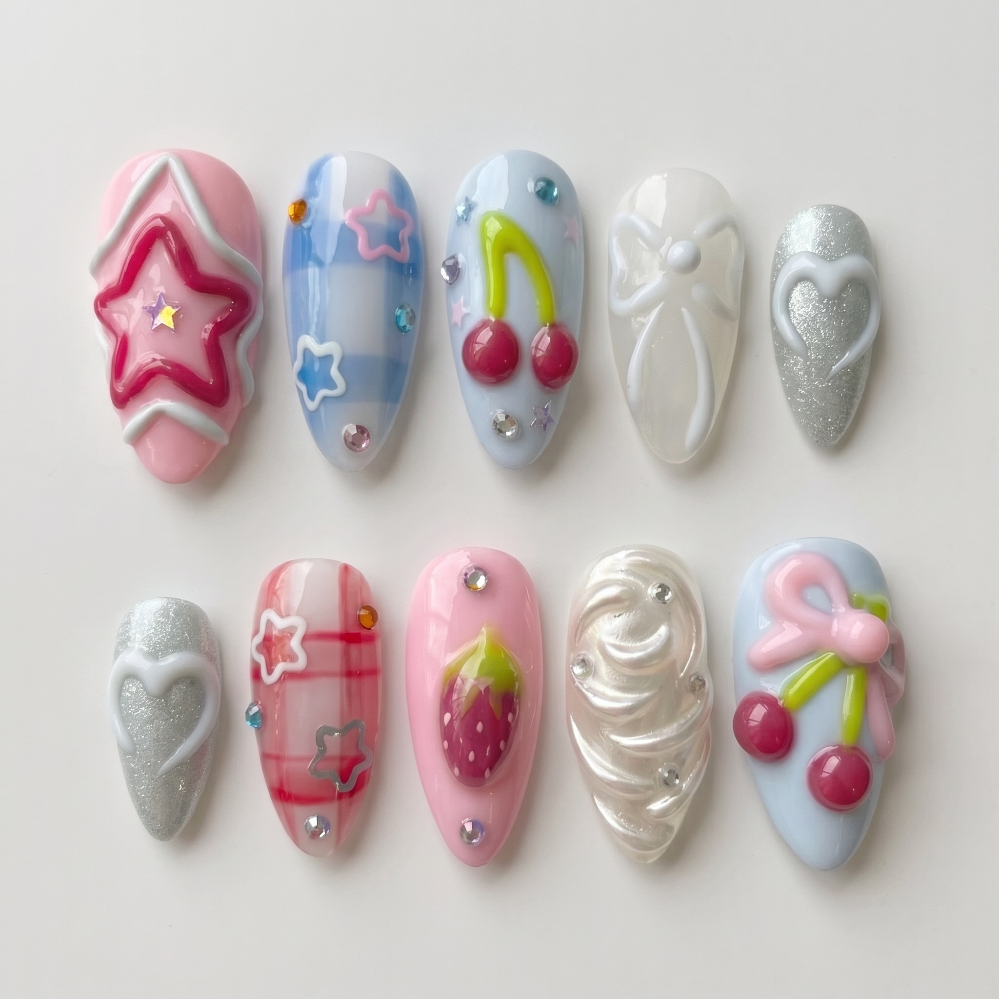 A set of pastel pink and blue press-on nails featuring 3D cherries, strawberries, bows, stars, and silver glitter hearts.