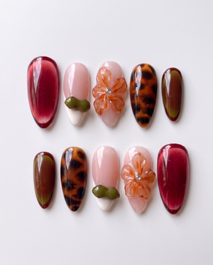 A set of press-on nails featuring burgundy cat-eye, tortoiseshell patterns, and 3D floral accents.