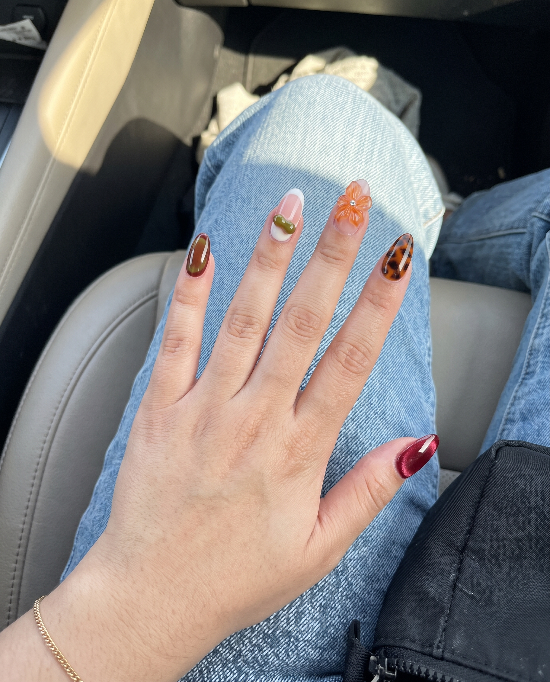 A set of press-on nails featuring burgundy cat-eye, tortoiseshell patterns, and 3D floral accents.
