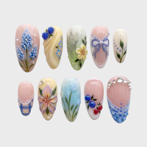 Mismatched pastel press-on nails featuring 3D blue flowers, berries, tulips, a silver butterfly, bows, and rhinestone embellishments.
