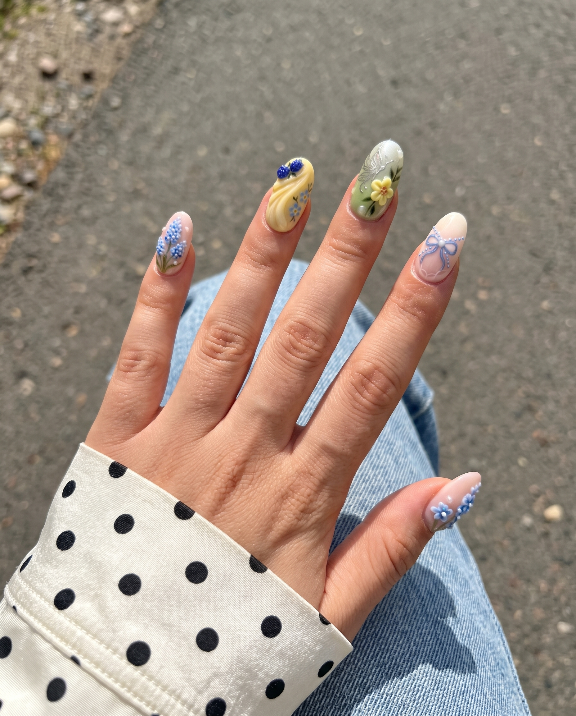 Mismatched pastel press-on nails featuring 3D blue flowers, berries, tulips, a silver butterfly, bows, and rhinestone embellishments.