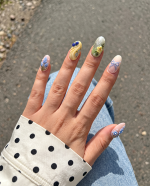 Mismatched pastel press-on nails featuring 3D blue flowers, berries, tulips, a silver butterfly, bows, and rhinestone embellishments.