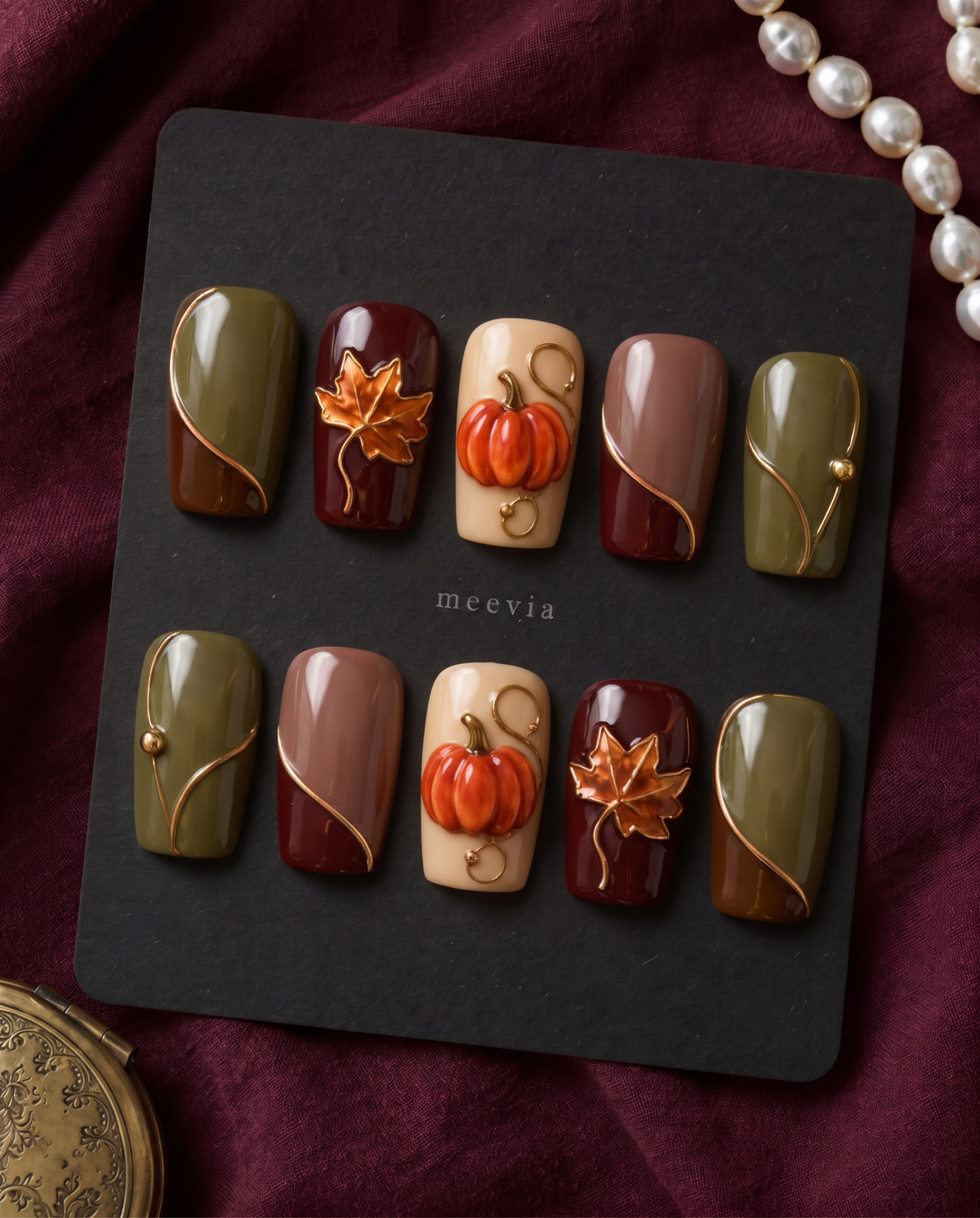 Autumn pumpkin and maple leaf press-on nails in glossy olive, burgundy, brown, mauve, and cream tones with gold accents
