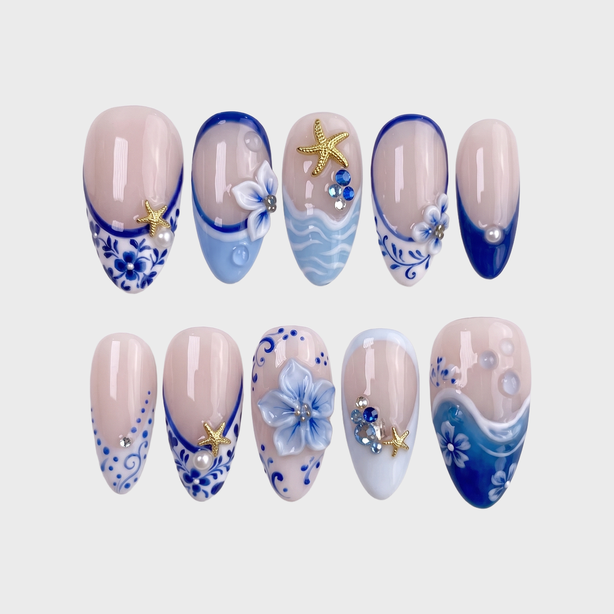 A set of ten press-on nails with blue and white floral patterns, gold starfish charms, pearls, and blue gems against a white background.