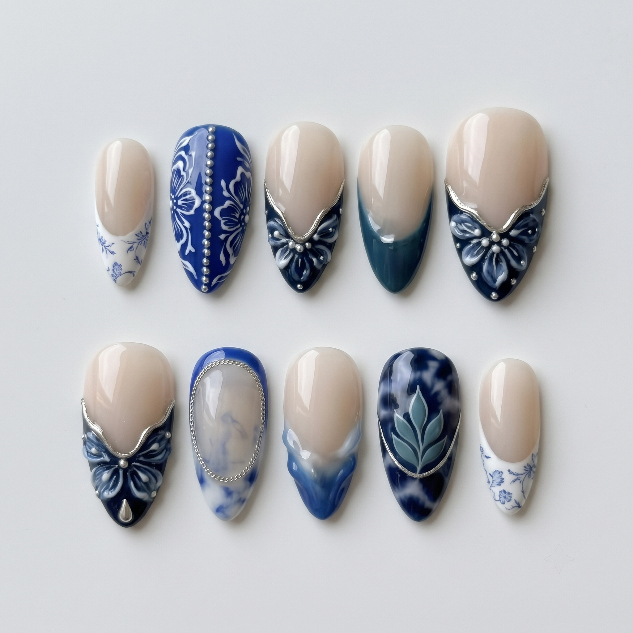 A set of blue and white porcelain-style press-on nails featuring floral patterns, marble designs, and silver accents.