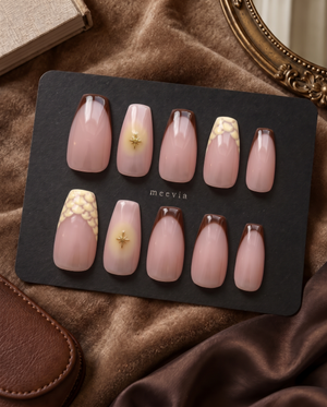 Glossy pink nude press-on nails with brown French tips, gold starburst accents, and cream floral details