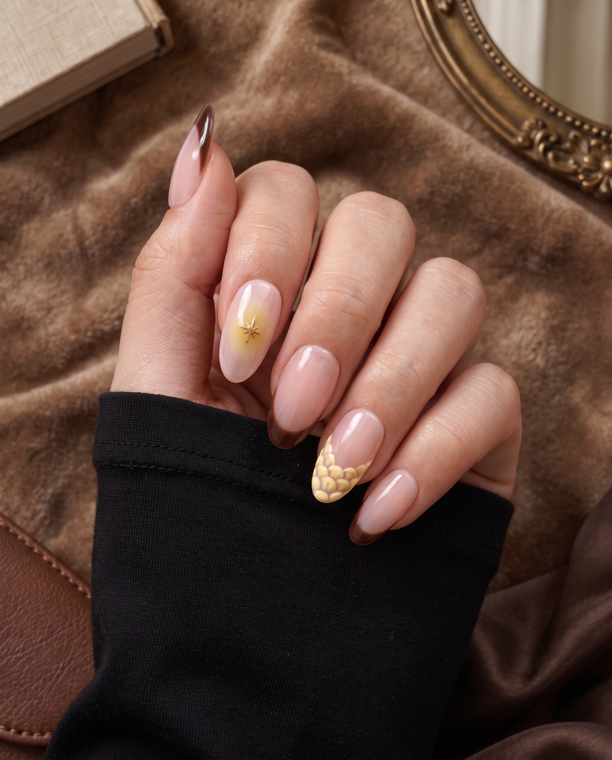 Glossy pink nude press-on nails with brown French tips, gold starburst accents, and cream floral details