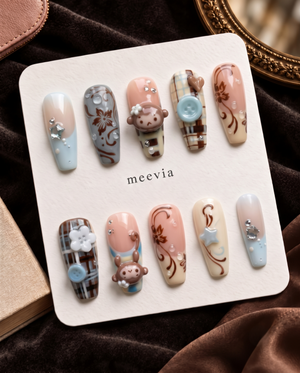 Brown plaid press-on nails with monkey charms, floral details, blue buttons, and rhinestone accents